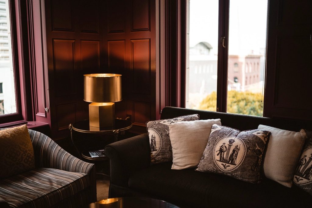 The Wexley lounge at dusk — velvet sofas and a brass lamp by the tall windows